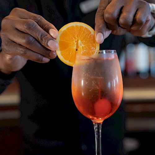 A bartender adds an orange slice to a cocktail in a stem glass, creating a visually appealing presentation.