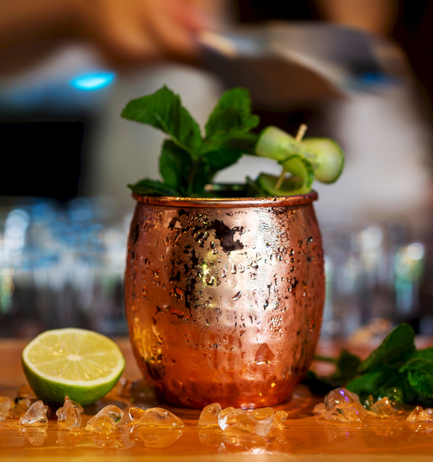 A copper mug with mint leaves and a lime wedge, surrounded by ice and a cut lime, on a table.