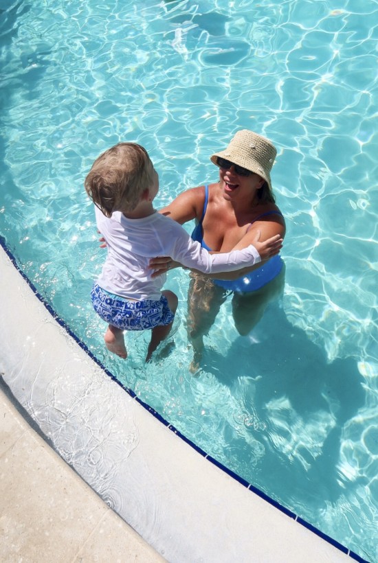 A woman and a child enjoy a joyful moment in the swimming pool, smiling and embracing each other on a sunny day.