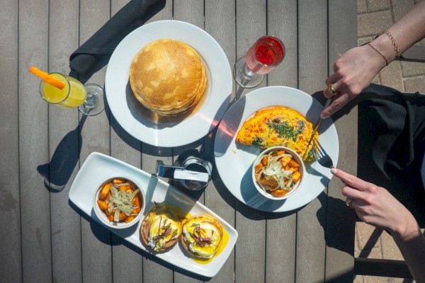 A meal with pancakes, an omelette, sweet potato fries, avocado toast, and drinks on a wooden table.