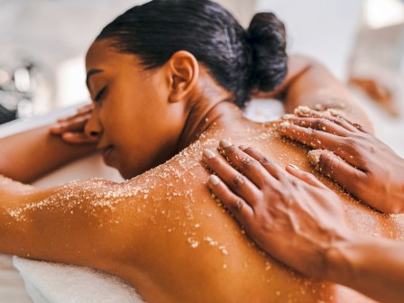 A person is receiving a relaxing back scrub massage, lying on a towel, with exfoliant applied to their skin.