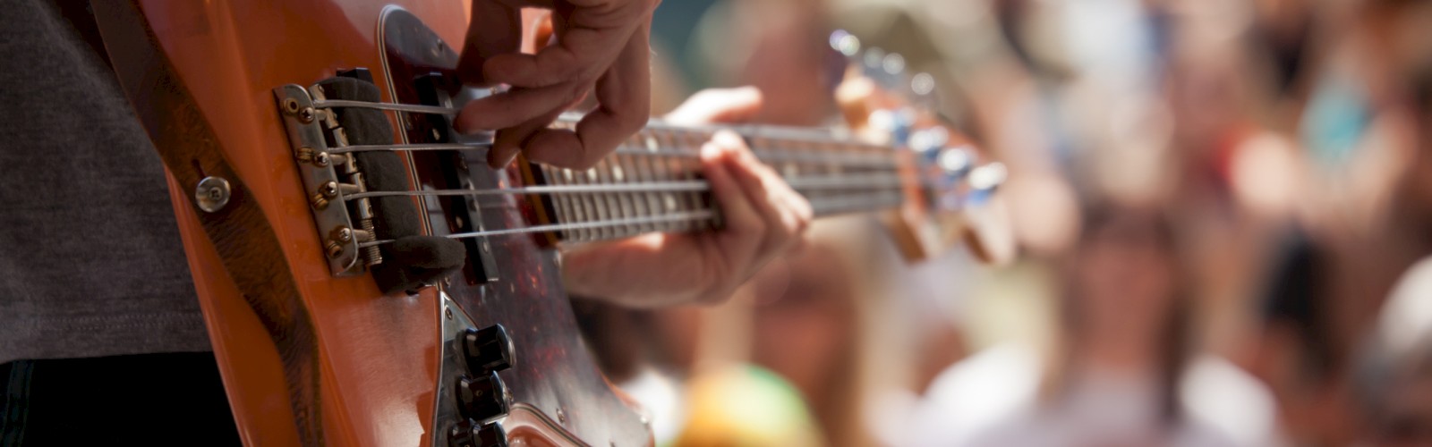 A person is playing an electric bass guitar in front of a crowd at an outdoor event.