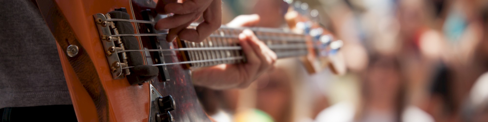 A person is playing an electric bass guitar in front of a crowd at an outdoor event.