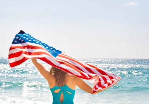 A woman holding an American flag on the beach during sunny weather with the ocean in the background.
