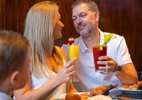 A couple is enjoying drinks at a table, with a child nearby. The table has breakfast items like muffins and a banana.