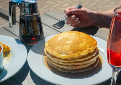 A table spread with pancakes, eggs Benedict, a salad, and drinks during breakfast outside.