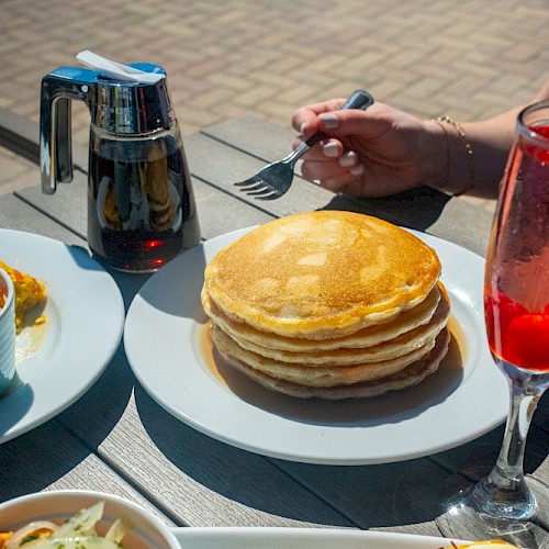 A table spread with pancakes, eggs Benedict, a salad, and drinks during breakfast outside.