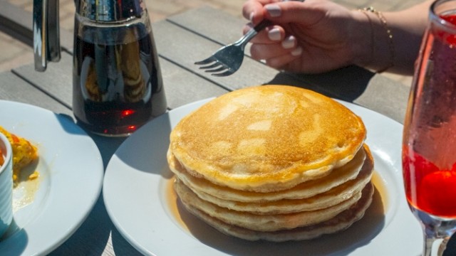 A table spread with pancakes, eggs Benedict, a salad, and drinks during breakfast outside.