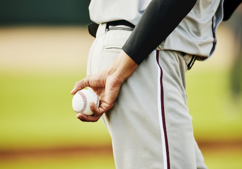 A person in a baseball uniform is holding a baseball behind their back on a field.