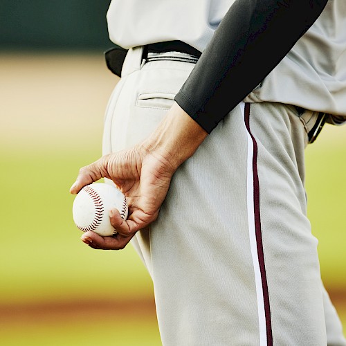 A person in a baseball uniform is holding a baseball behind their back on a field.