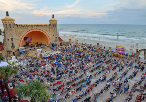 A large crowd is gathered by a seaside amphitheater with an arch, attending an event or concert, with the ocean visible in the background.