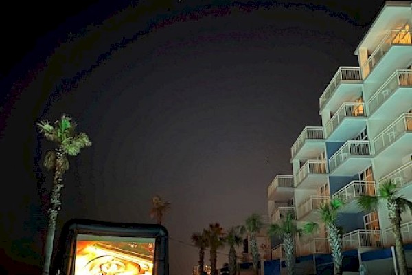 A nighttime outdoor movie setup by a pool, surrounded by palm trees and a multi-story building with balconies.