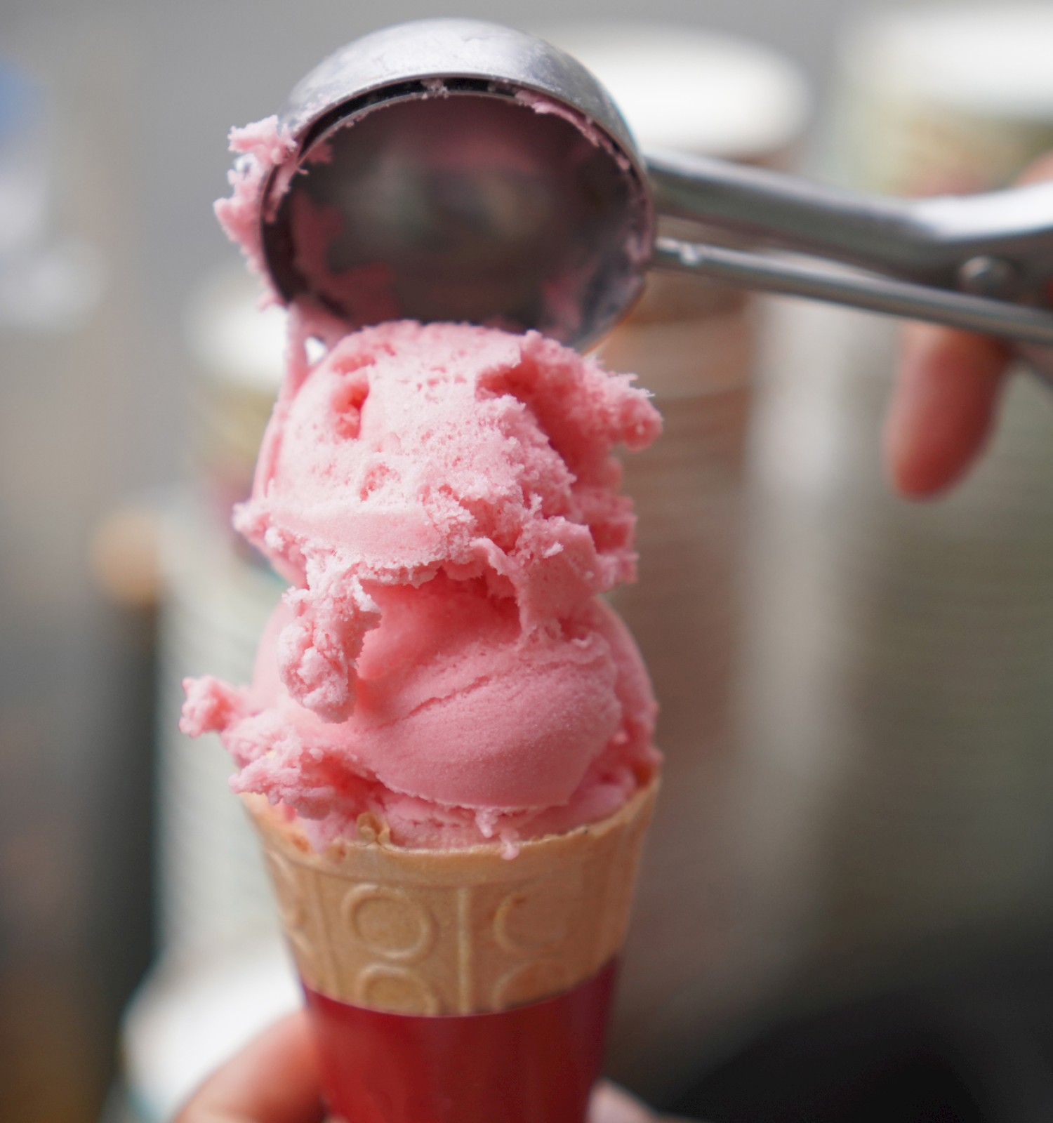 A close-up of a pink ice cream being scooped onto a cone with a metal scooper.