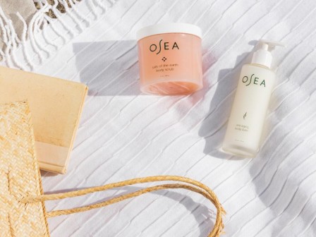 Beach-ready skincare products, a woven bag, and towel on the sand suggest a relaxing day by the sea.
