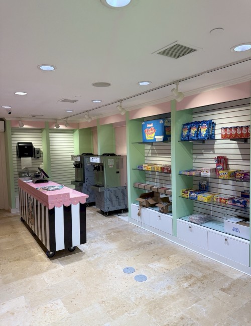 A small store with shelves stocked with snacks and candy, a counter with a pink cover, and a coffee machine.