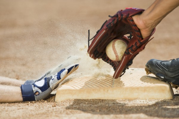 A baseball player slides into a base while another player tags with a glove and ball. Dust is kicked up around them.