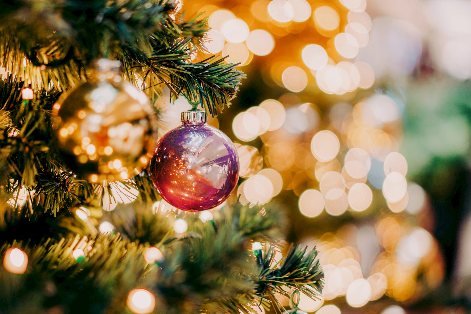 A close-up of a Christmas tree with shiny ornaments and warm bokeh lights in the background.