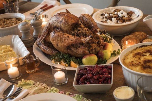 A Thanksgiving feast with a roast turkey, stuffing, mashed potatoes, cranberry sauce, gravy, and side dishes on a wooden table.