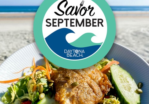 A plate of food with fish, salad, cucumbers, and tomatoes is in front of a beach. The 