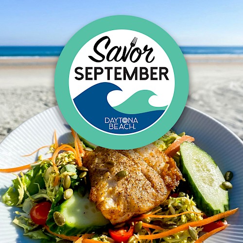 A plate of food with fish, salad, cucumbers, and tomatoes is in front of a beach. The 