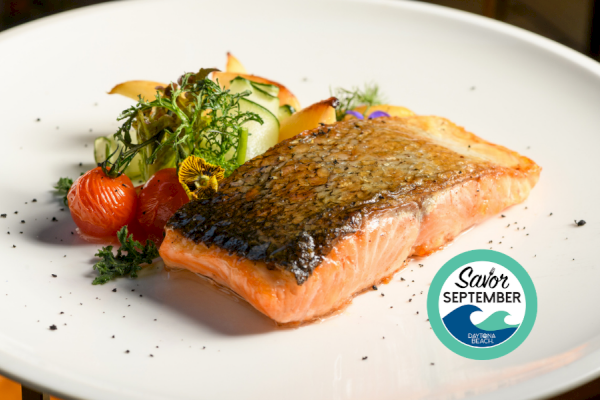 A plated dish featuring grilled salmon with crispy skin, accompanied by fresh vegetables and garnished, promoting September dining at Daytona Beach.