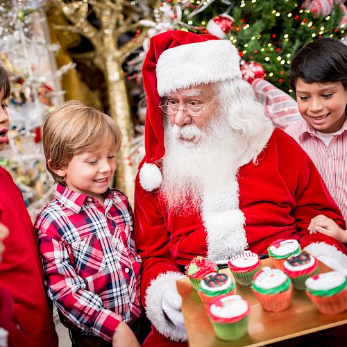 Santa Claus shows kids decorated Christmas cupcakes at a festive holiday gathering.