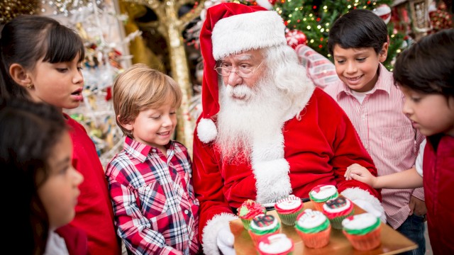 Santa Claus shows kids decorated Christmas cupcakes at a festive holiday gathering.