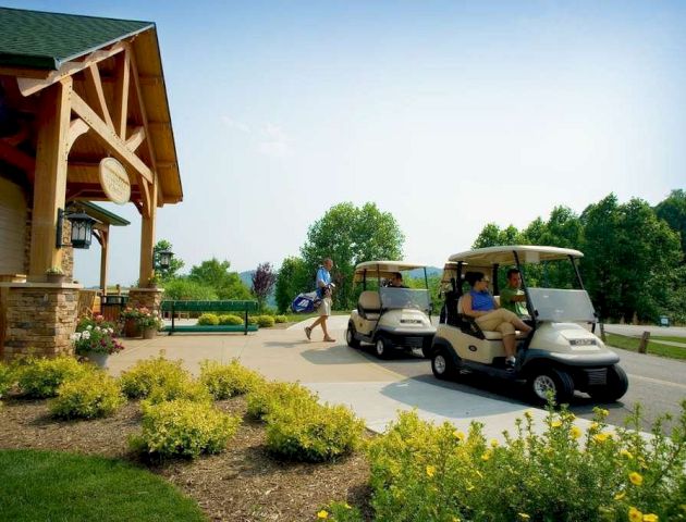 The image shows people near golf carts outside a building with flower beds and greenery. The scene appears bright and clear, indicating a sunny day.