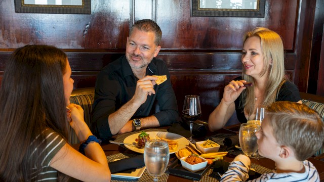 A family gathers around a table at a restaurant, sharing drinks and appetizers while chatting and smiling at each other.