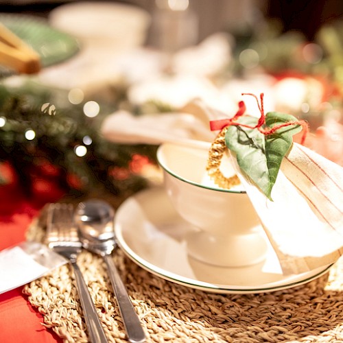 The image shows a festive table setting with holiday-themed decorations, including a white bowl with a holiday ornament and napkin.
