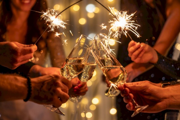 A group cheers with sparklers, clinking champagne flutes in a celebratory toast at a festive party.