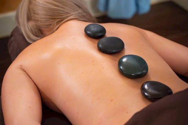 A person lying face down getting a hot stone spa massage with smooth stones along the back, dim cozy room, and towels.