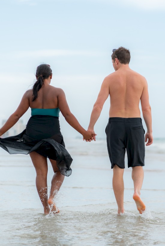 A couple walks hand-in-hand along the shoreline, enjoying a sunny day at the beach.