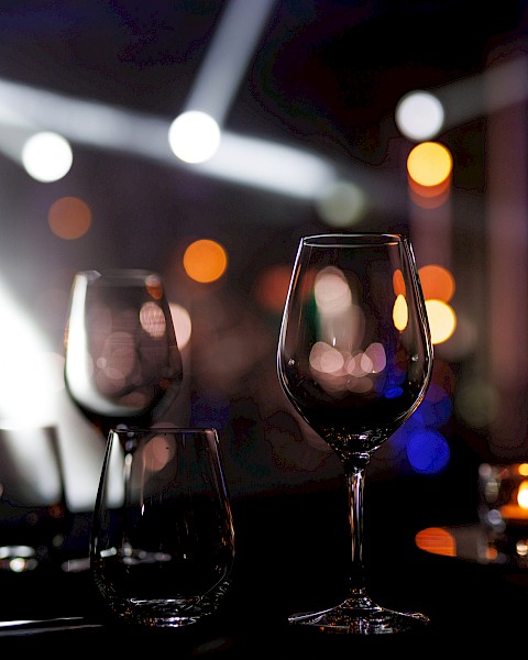 Two empty wine glasses on a table with soft candlelight and bokeh orbs in a dim, chic restaurant or bar setting. End with a period.