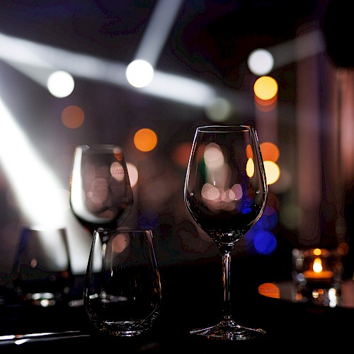 Two empty wine glasses on a table with soft candlelight and bokeh orbs in a dim, chic restaurant or bar setting. End with a period.