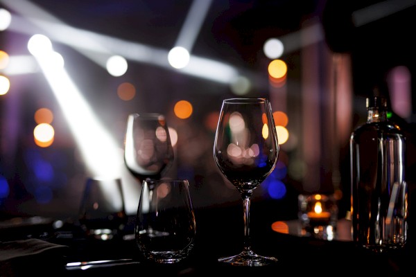 Two wine glasses on a table in a dimly lit, elegant restaurant with bokeh lights in the background.